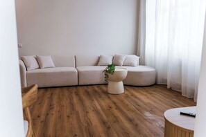 A modern living room with a curved sofa, a round coffee table with a plant, and wooden flooring. - Design apartment by the park with parking (Celle)