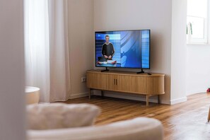 A modern living room with a flat-screen TV mounted on a wooden console, a white sofa, and a wooden floor. - Design apartment by the park with parking (Celle)