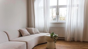 A minimalist living room with a beige sofa, a round side table with a plant, and a window with sheer curtains. - Design apartment by the park with parking (Celle)