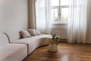 A minimalist living room with a beige sofa, a round side table with a plant, and a window with sheer curtains. - Design apartment by the park with parking (Celle)