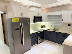A modern kitchen with a stainless steel refrigerator, a microwave, a gas stove, and a sink. - Modern Luxury Apartment in Baní (Baní)