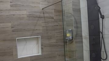Eine begehbare, gläserne Dusche mit modernem Design, Bedienfeld und einer kleinen Ablagefläche.
