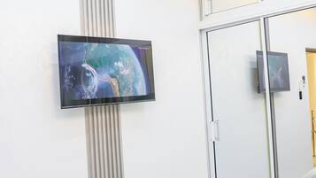 Un dormitorio moderno con una televisión de pantalla plana montada en la pared, una cama con cabecera gris y un espejo grande que refleja la habitación.
