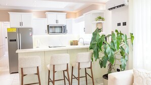 A modern kitchen with white cabinetry, a built-in microwave, and a bar area with stools. - Modern Luxury Apartment in Baní (Baní)