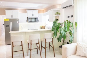 A modern kitchen with white cabinetry, a built-in microwave, and a bar area with stools. - Modern Luxury Apartment in Baní (Baní)