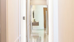A corridor with a reflective floor leading to a room with a wooden door and a small plant on a table. - Modern Luxury Apartment in Baní (Baní)