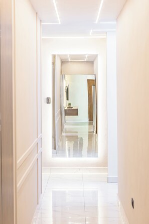 A corridor with a reflective floor leading to a room with a wooden door and a small plant on a table. - Modern Luxury Apartment in Baní (Baní)