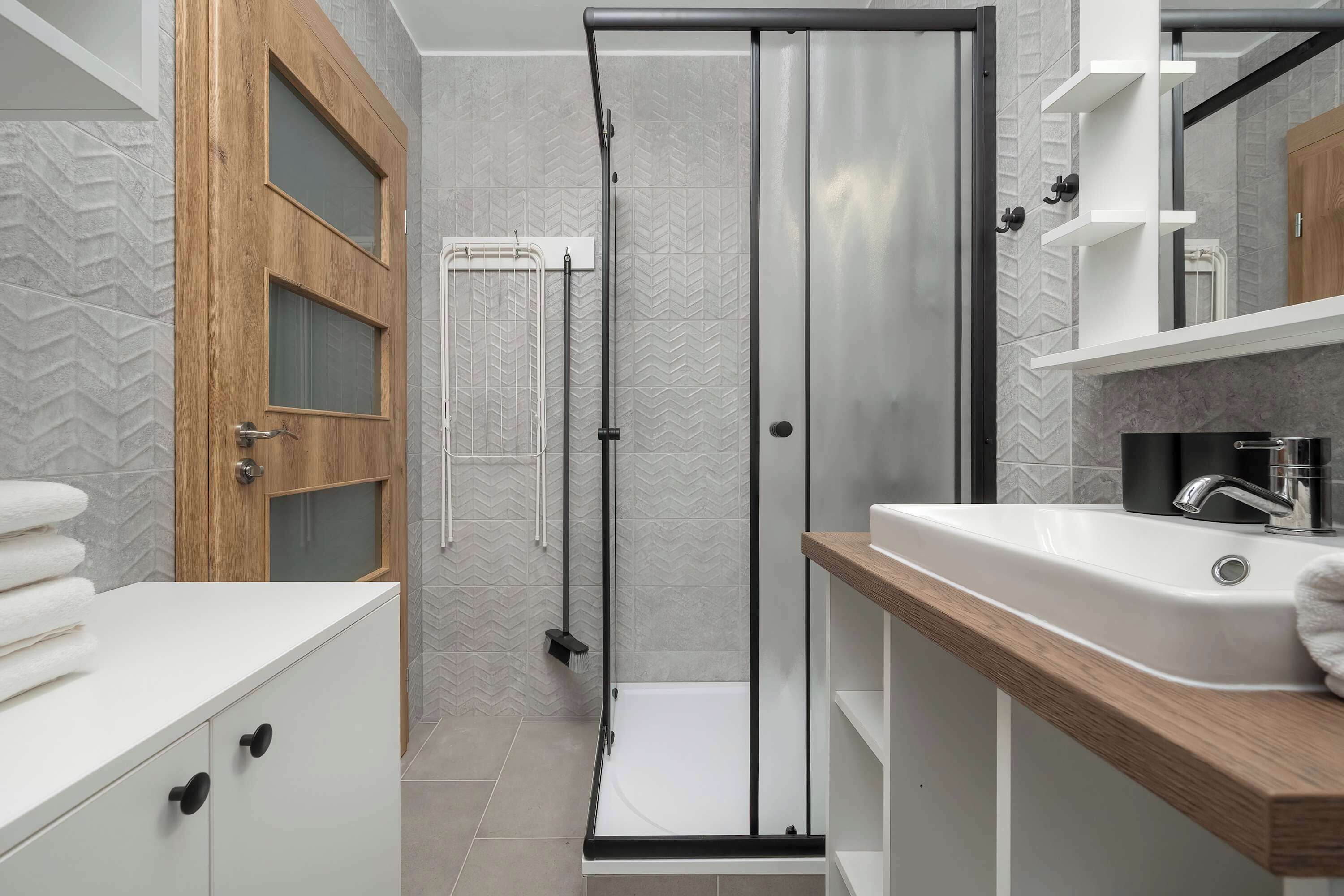 A modern bathroom with a glass-enclosed shower, a wooden vanity, and a white sink.