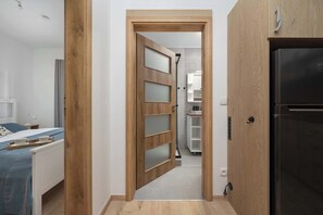 Habitación de hotel con cama, puerta de madera con paneles de vidrio esmerilado, refrigerador negro y baño con espejo y estanterías.
