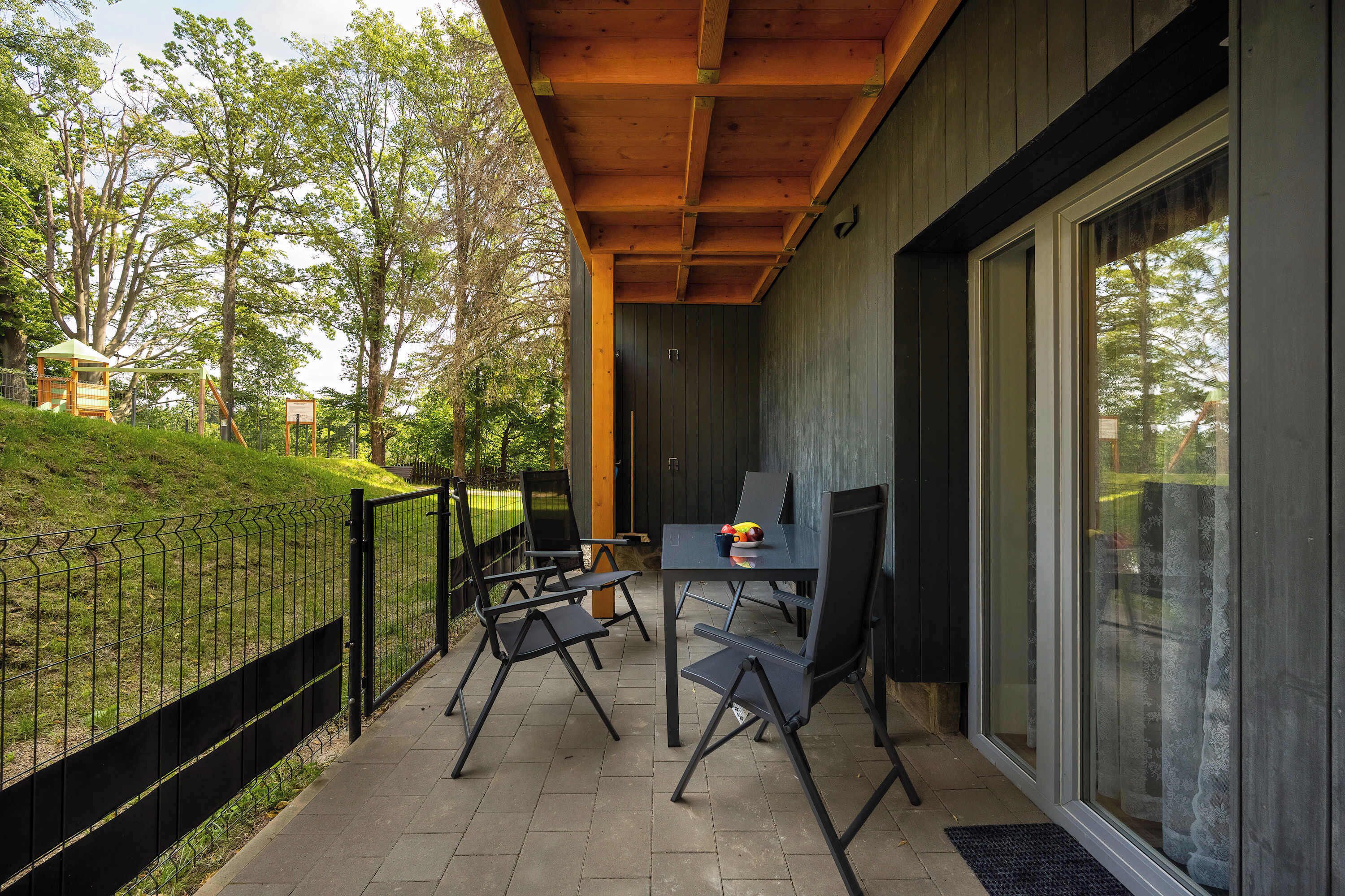 A covered outdoor seating area with a table and chairs, a wooden ceiling, and a view of a grassy area with trees.