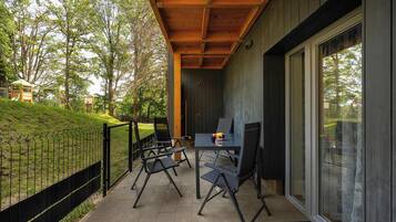 A covered outdoor seating area with a table and chairs, a wooden ceiling, and a view of a grassy area with trees.