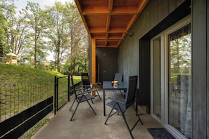 A covered outdoor seating area with a table and chairs, a wooden ceiling, and a view of a grassy area with trees.