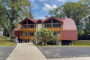 Un edificio de dos pisos con techo rojo, balcones de madera y entrada pavimentada.