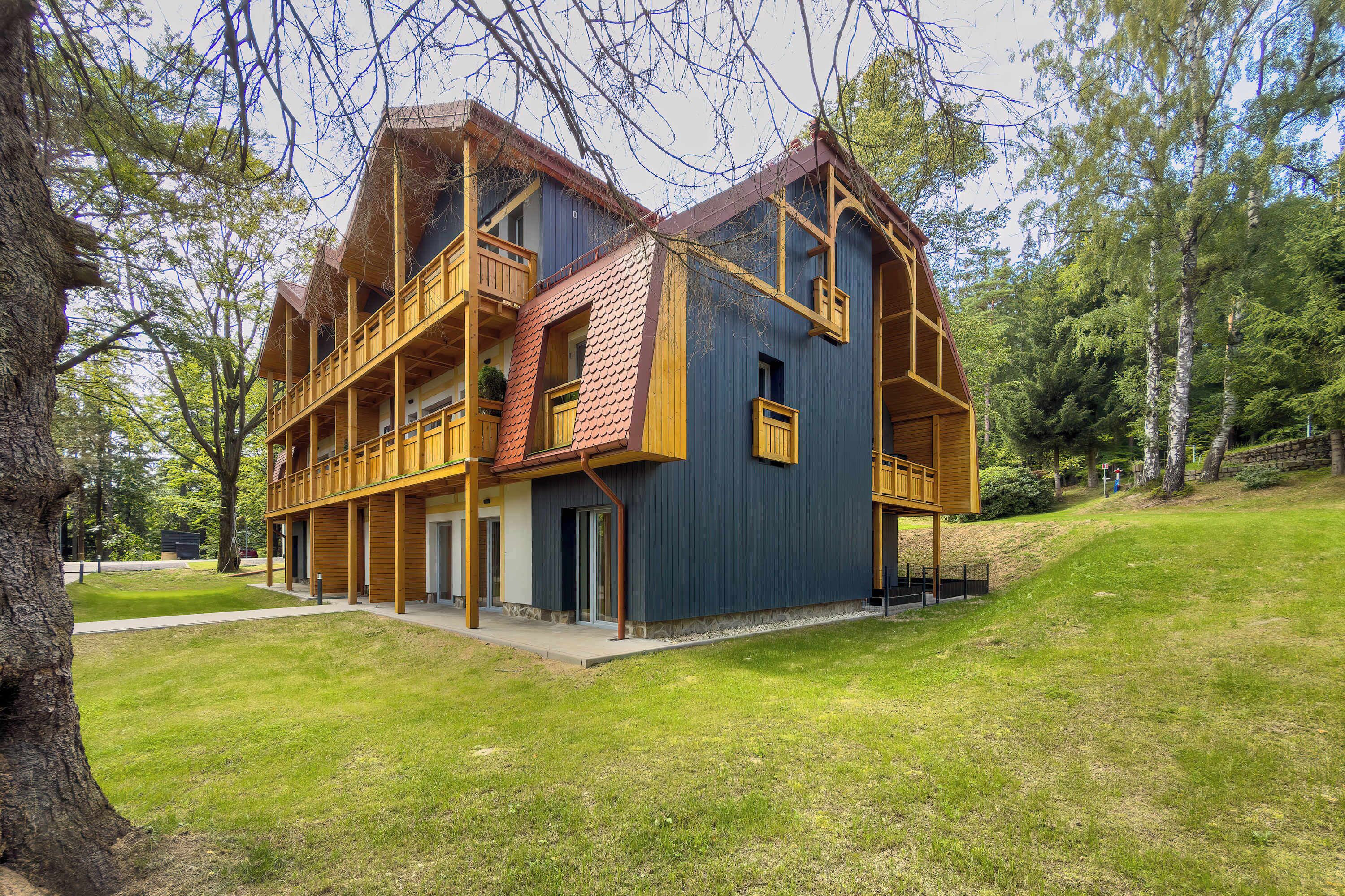 A two-story wooden building with balconies, surrounded by trees and a grassy area.