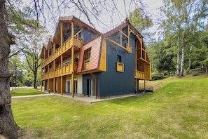A two-story wooden building with balconies, surrounded by trees and a grassy area.
