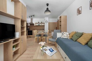 Una sala moderna con televisor de pantalla plana, un sofá, una mesa de centro con una revista y un comedor con una mesa y sillas.
