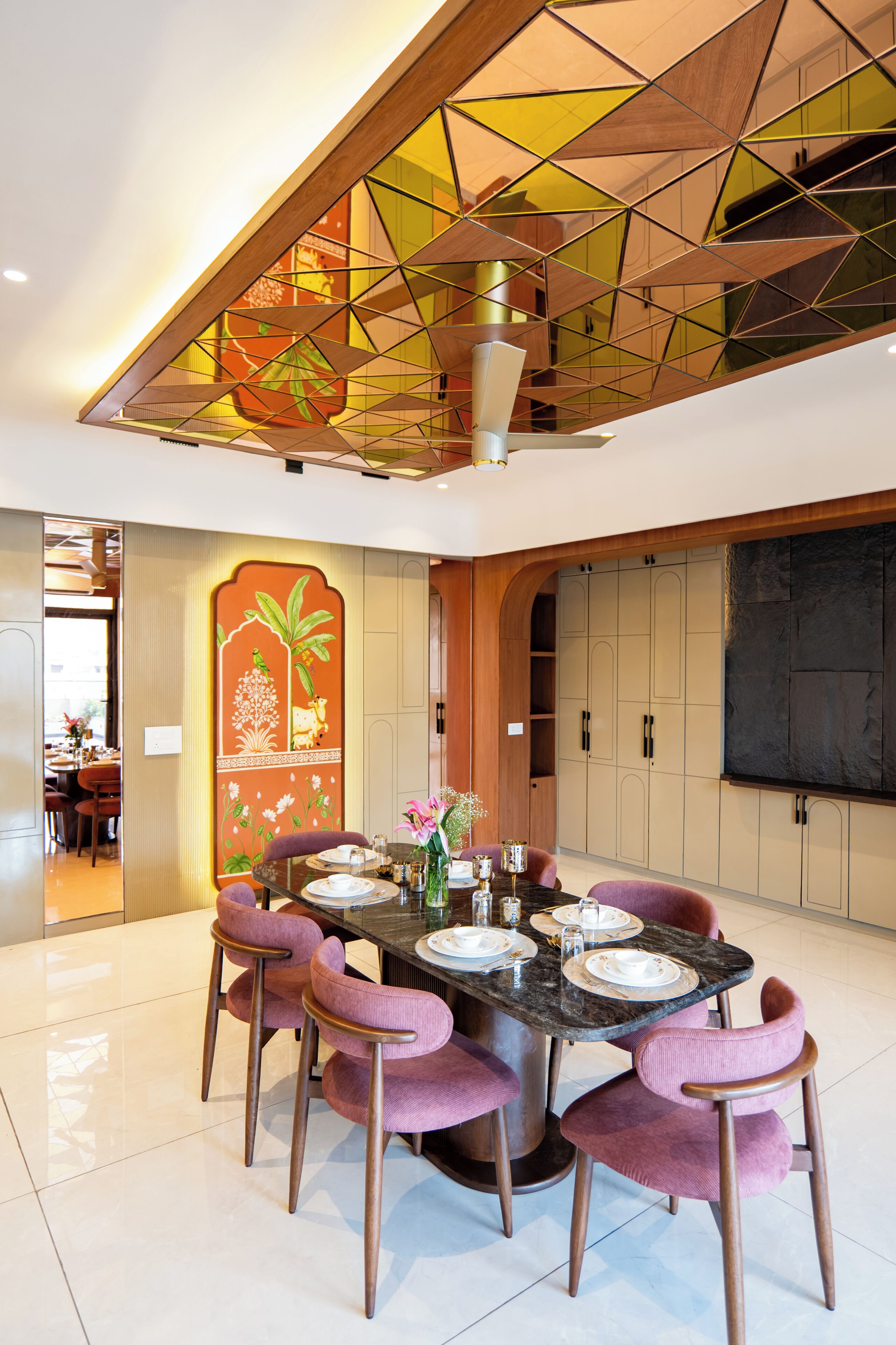 A dining area with a round table, pink chairs, and a decorative wall with a tropical mural.
