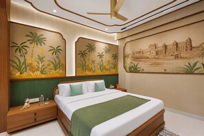 Quarto de hotel com uma cama grande, mesa de cabeceira, manta verde, painel na parede com palmeiras e ventilador de teto.