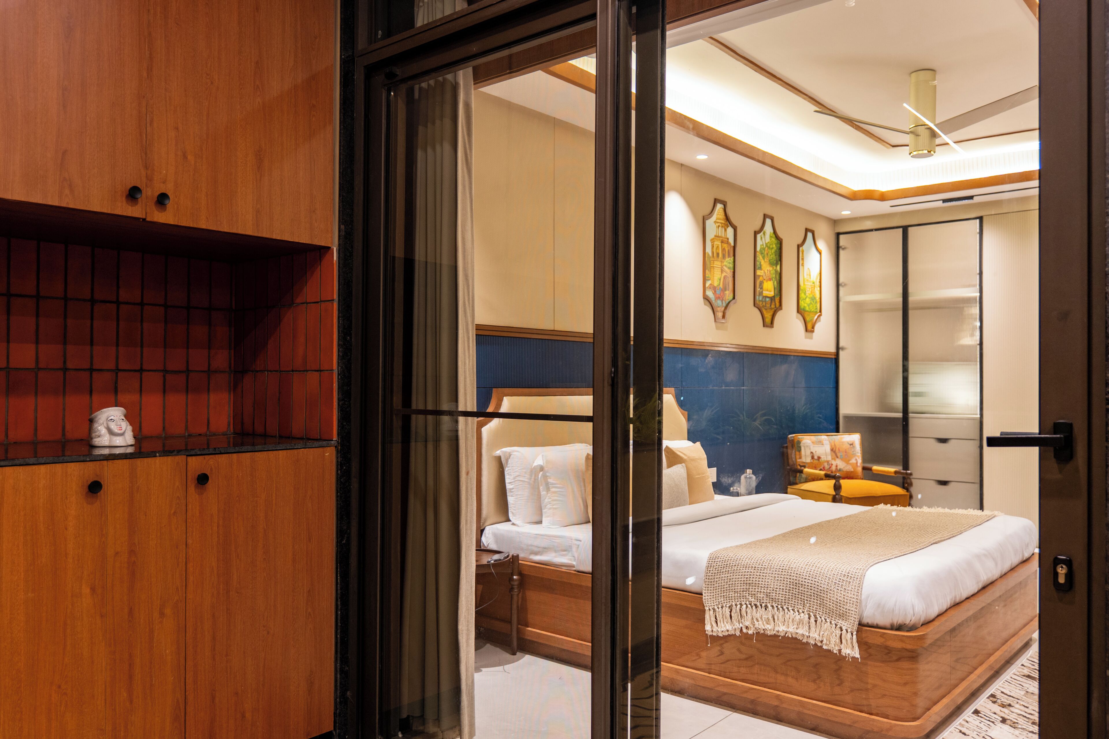 Une chambre d’hôtel moderne avec une armoire en bois, un lit avec du linge de maison blanc, une table de chevet et une lampe fixée au mur.