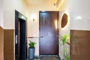Entrada de hotel com porta de madeira escura, elevador digital e um vaso de planta.