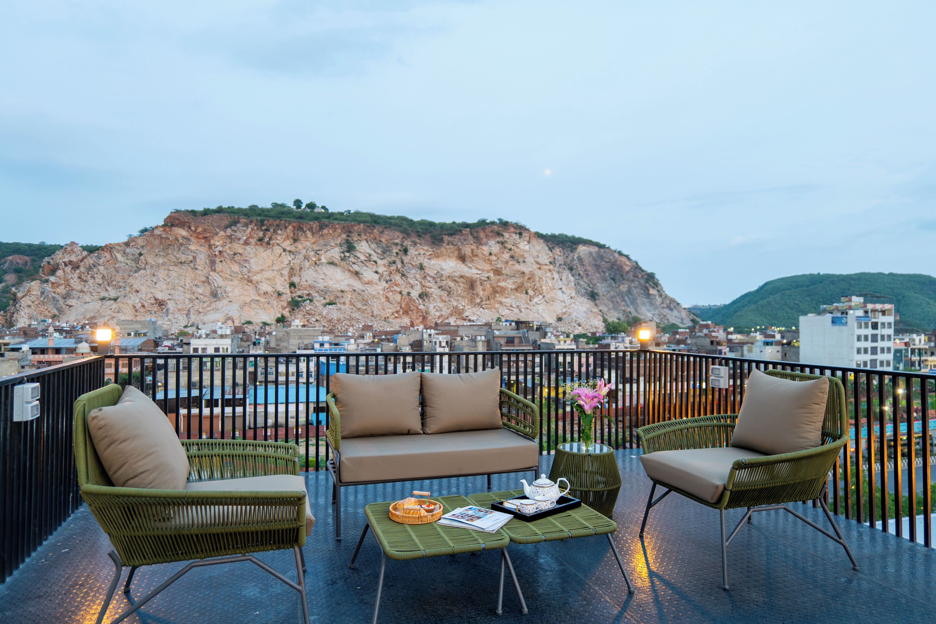A balcony with wicker furniture, a small table, and a view of a cityscape and a mountain.