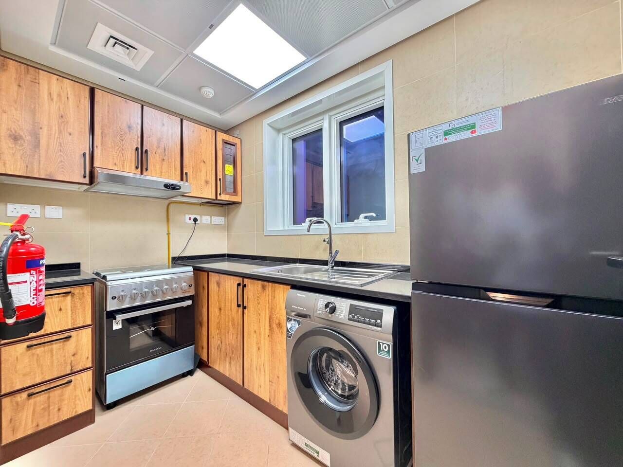 Una cocina con armarios de madera, un refrigerador de acero inoxidable, una lavadora y una estufa a gas.