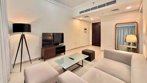 Una sala moderna con sofá, una mesa de centro, un televisor sobre un mueble, una lámpara y una ventana con cortinas.