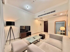 Una sala moderna con sofá, una mesa de centro, un televisor sobre un mueble, una lámpara y una ventana con cortinas.