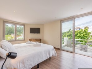 Ein modernes Schlafzimmer mit einem großen Bett, einem Flachbildfernseher und einem Balkon mit Sitzmöbeln.
