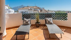A terrace with two lounge chairs, a potted plant, and a view of a mountain and buildings. - Se or o de Aloha in Marbella (Marbella)
