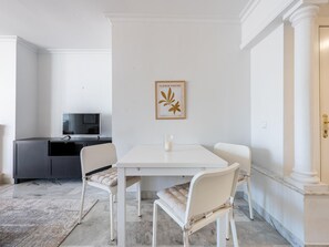 Ein moderner Essbereich mit einem weißen Tisch und Stühlen, einem gerahmten Kunstwerk an der Wand und einem Fernseher im Hintergrund.