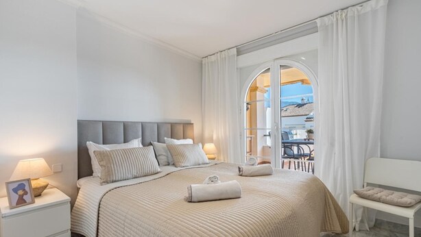 A bedroom with a large bed, a nightstand, a chair, and a view of the outdoors through a glass door. - Se or o de Aloha in Marbella (Marbella)