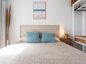 Ein Schlafzimmer mit einem Bett, Kissen, einem Nachttisch, einer Lampe und einem gerahmten Bild an der Wand.