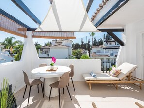 A rooftop terrace with a round table, chairs, a lounge chair, and a view of neighboring buildings. - Los Naranjos Modern 2 Bedroom Penthouse With Views (Marbella)
