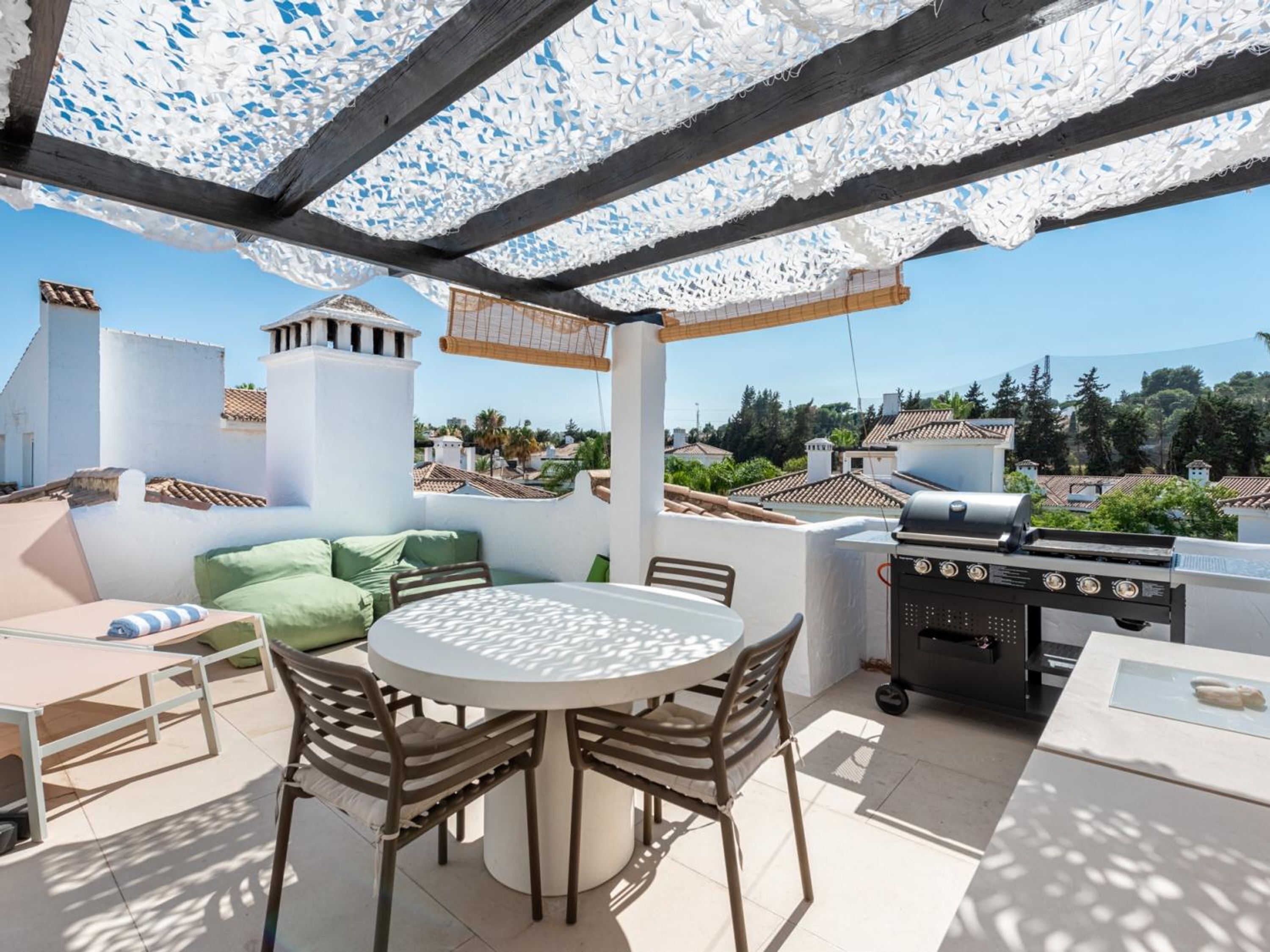 Eine Terrassengruppe im Freien mit rundem Tisch, Stühlen, einem Grill und Blick auf die umliegende Nachbarschaft.