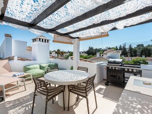 An outdoor patio with a round table, chairs, a grill, and a view of the surrounding neighborhood. - Los Naranjos Modern 2 Bedroom Penthouse With Views (Marbella)