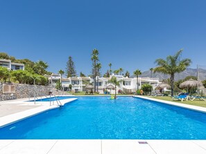 Ein Swimmingpool mit klarem, blauem Wasser, umgeben von weißen Gebäuden, Palmen und einem Berg im Hintergrund.