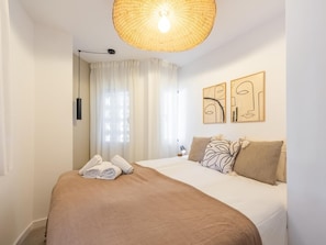 Ein Hotelzimmer mit einem Bett, einer Pendelleuchte, einem Fenster mit Vorhängen und zwei Wandbildern.