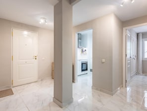 A modern interior with a marble floor, a white door, and a kitchen area visible through an open door. - Azahara1 Mountain Views and Frontline Golf (Marbella)