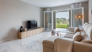 A modern living room with a flat-screen TV, a sofa, a coffee table, and a view of a green landscape through a glass door. - Azahara1 Mountain Views and Frontline Golf (Marbella)