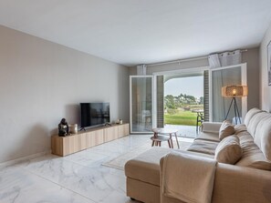 A modern living room with a flat-screen TV, a sofa, a coffee table, and a view of a green landscape through a glass door. - Azahara1 Mountain Views and Frontline Golf (Marbella)