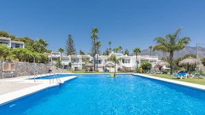 A swimming pool with a clear blue water, surrounded by white buildings, palm trees, and a mountain in the background. - Azahara1 Mountain Views and Frontline Golf (Marbella)