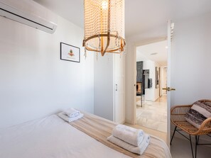 Ein Hotelzimmer mit einem Bett, einer Pendelleuchte, einer Tür zu einem Flur und einem Korbstuhl.