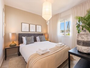 A hotel room with a bed, bedside lamps, a large window with curtains, a view of the outside, and three framed pictures on the wall. - Los Naranjos Modern 3 Bedroom Penthouse (Marbella)