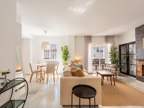 Ein modernes Wohnzimmer mit einer Couch, einem Esstisch, Stühlen, einem Kamin und Blick durch eine Glastür.