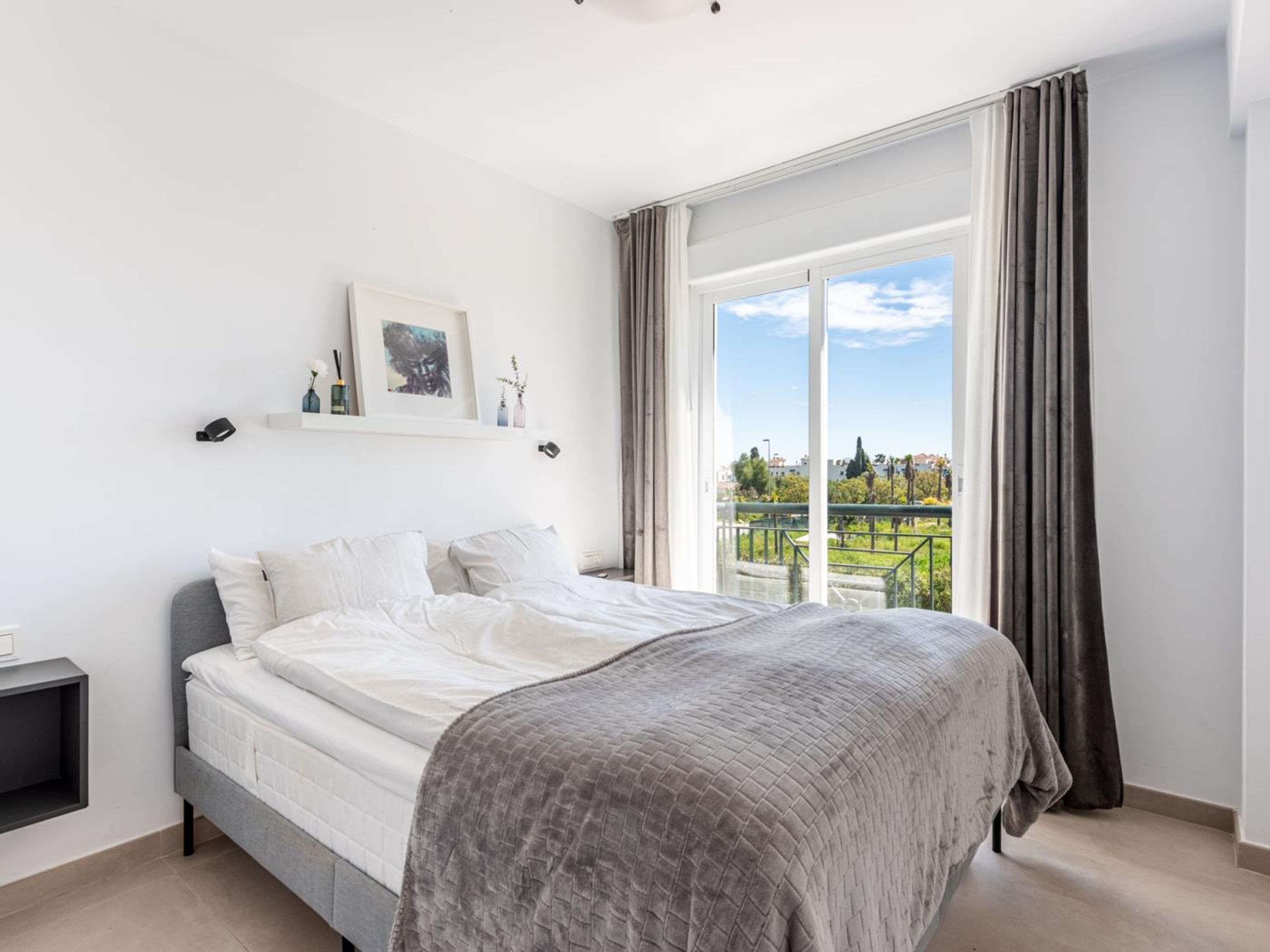 A modern bedroom with a large bed, a small bedside table, and a window with curtains.