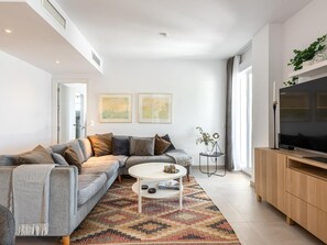 A modern living room with a grey sofa, a round coffee table, and a TV on a wooden cabinet. - Locrimar Family Apartment With Amazing Location (Marbella)