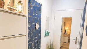 A hallway with a patterned wall, a door with a mirror, a small plant, and a rug with an anchor design. - Küstenblick by Interhome (Burhave)