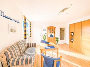 A living room with a striped sofa, a dining table with chairs, a wooden cabinet, and a wardrobe. - Meeresrauschen by Interhome (Burhave)