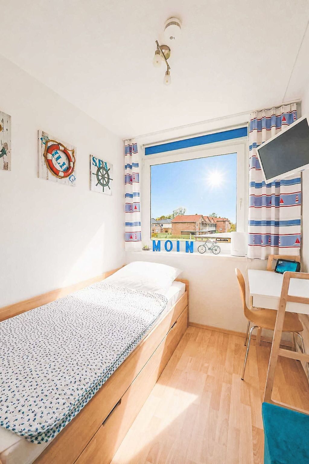 Een kamer met een bed, een bureau, een stoel, een raam met uitzicht en nautische decoraties.
